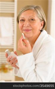 Senior woman in bathroom looking at camera cleaning facial cream
