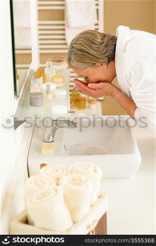 Senior woman in bathroom washing her face at wash basin