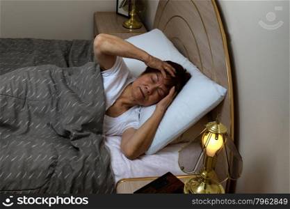 Senior woman, in bed, holding her head while in pain during night time. Insomnia concept.