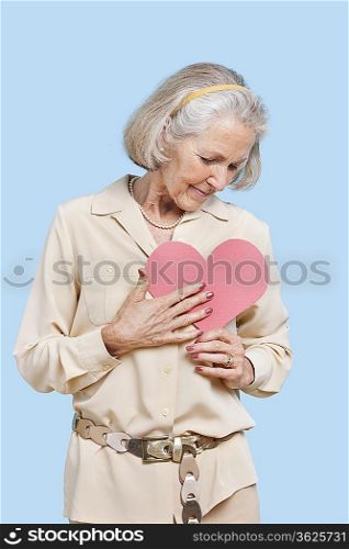 Senior woman in casuals holding red paper heart against blue background