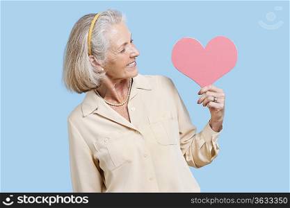 Senior woman in casuals holding red paper heart against blue background