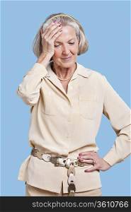 Senior woman in casuals suffering from headache against blue background