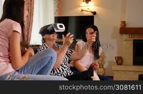 Senior woman in virtual reality headset or 3d glasses having fun with her granddaughters. Senior woman wearing virtual reality glasses at home. People having fun with new technology concept. Slow motion