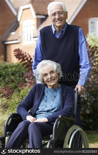 Senior Woman In Wheelchair Being Pushed By Husband