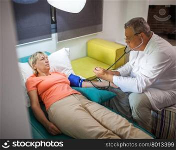Senior woman is under doctor control at home. Man checking blood pressure using tonometer and stethoscope. Doctor measuring blood pressure of woman at home