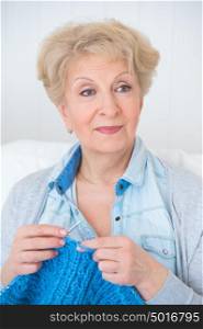 Senior woman knitting on her sofa at home