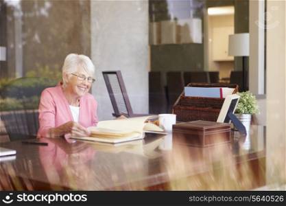 Senior Woman Looking At Photo Album Through Window