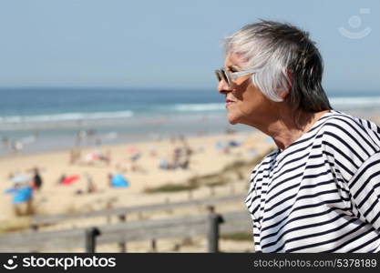 Senior woman looking out over a sandy beach on a summer day