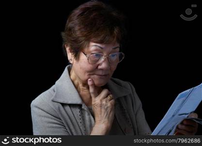 Senior woman looking surprised by her bills. Black background.