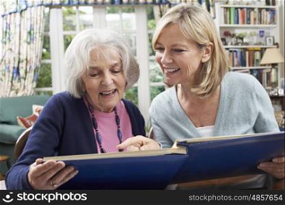 Senior Woman Looks At Photo Album With Mature Female Neighbor