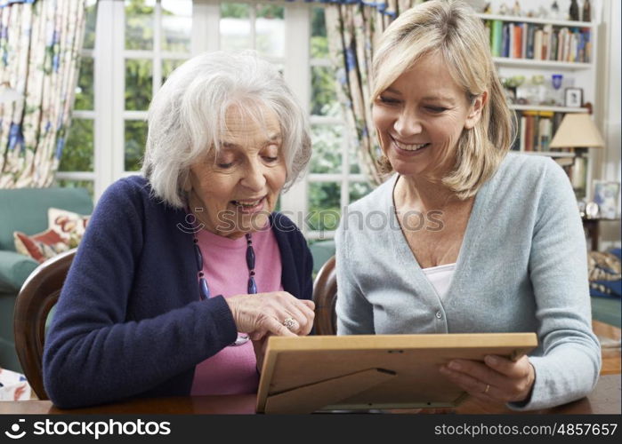 Senior Woman Looks At Photo Frame With Mature Female Neighbor