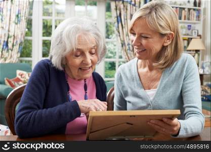 Senior Woman Looks At Photo In Frame With Mature Female Neighbor