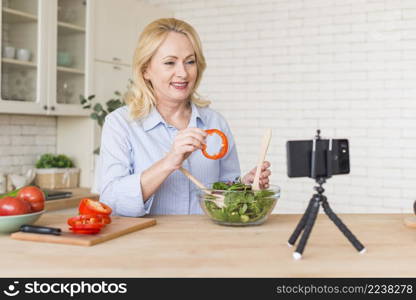 senior woman making video call mobile phone showing bell pepper slice while preparing salad