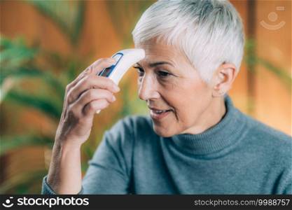 Senior Woman Measuring Body Temperature with Contactless Digital Thermometer at Home. Senior Woman Measuring Body Temperature with Contactless Digital Thermometer
