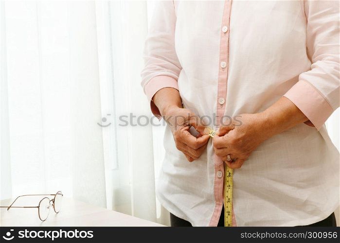 Senior woman measuring her waist by measuring tape