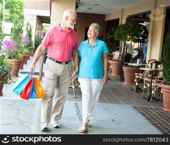 Senior woman on a shopping spree looks up at her handsome husband who&rsquo;s carrying her bags.