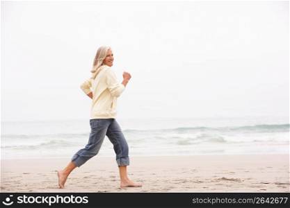 Senior Woman On Holiday Running Along Winter Beach