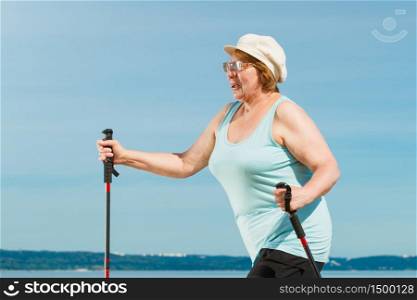 Senior woman practicing nordic walking on sea shore, Active elderly female enjoying sunny summer day. Healthy lifestyle in old age.. Senior woman practicing nordic walking on beach