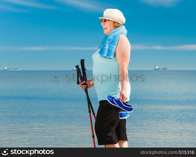 Senior woman practicing nordic walking on sea shore, Active elderly female enjoying sunny summer day. Healthy lifestyle in old age.. Senior woman practicing nordic walking on beach