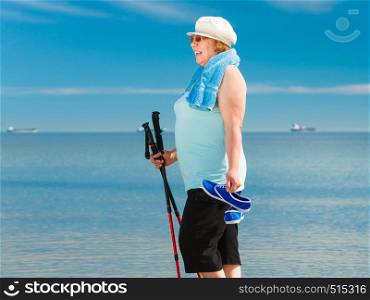 Senior woman practicing nordic walking on sea shore, Active elderly female enjoying sunny summer day. Healthy lifestyle in old age.. Senior woman practicing nordic walking on beach