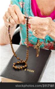 Senior woman praying the rosary with her beads and her bible. Shallow depth of field with focus on her fingers holding the beads.