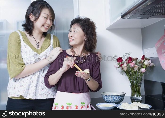 Senior woman preparing food with her granddaughter standing behind her and smiling