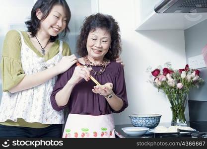 Senior woman preparing food with her granddaughter standing behind her and smiling