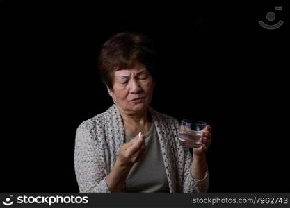 Senior woman preparing to take her medicine with water. Black background.