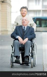 senior woman pushing man in wheelchair