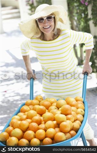 Senior Woman Pushing Wheelbarrow Filled With Oranges