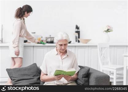 senior woman reading book front woman doing housekeeping work