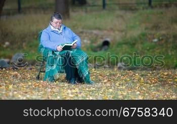 Senior woman reading book in autumn park Front View
