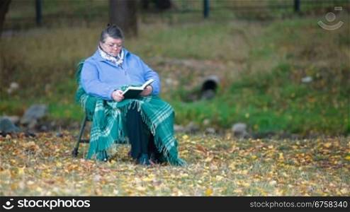 Senior woman reading book in autumn park Front View