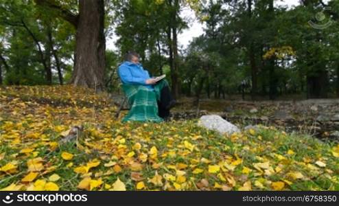 Senior Woman Reading Book in Autumn Park, Wide Angle, Dolly shot, Side View