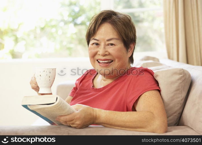 Senior Woman Reading Book With Drink At Home