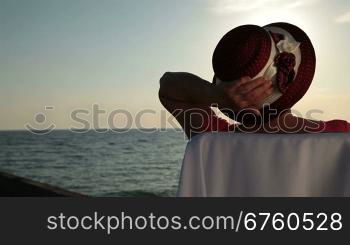 Senior woman relaxing by sea on the beach at sunset, rear view, tracking shot