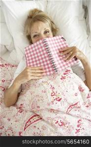 Senior Woman Relaxing In Bed Reading Diary