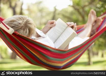 Senior Woman Relaxing In Hammock With Book