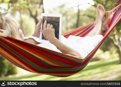 Senior Woman Relaxing In Hammock With E-Book