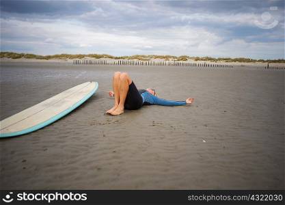 Senior woman relaxing on sand, surfboard beside her