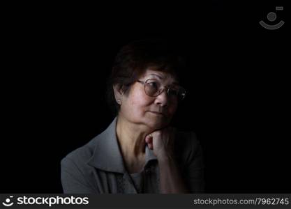 Senior woman resting her chin with one hand while displaying loneliness on black background. Depression concept.