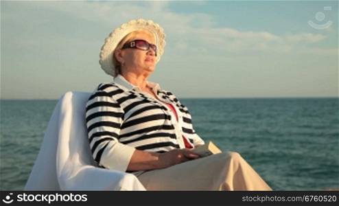 Senior woman resting on the seacoast at sunset, medium shot