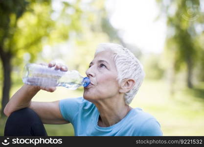 Senior woman rests and drinks water after workout in the park