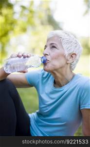 Senior woman rests and drinks water after workout in the park