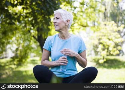 Senior woman rests and drinks water after workout in the park