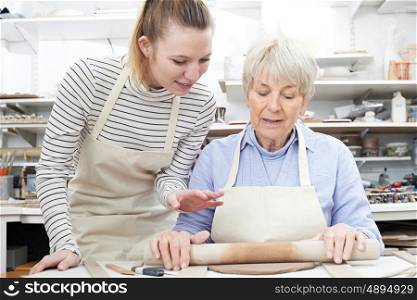 Senior Woman Rolling Out Clay With Teacher In Pottery Class