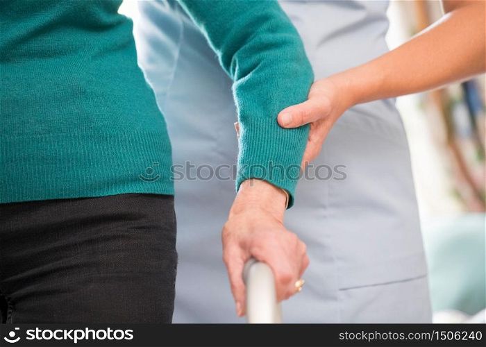 Senior Woman&rsquo;s Hands On Walking Frame With Care Worker In Background