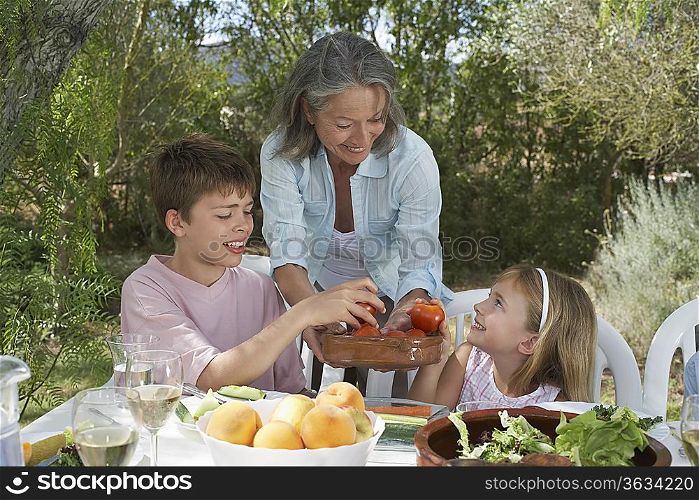 Senior woman serving fruit to children (6-11), in garden