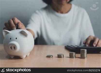 senior woman sitting at a table and saving her money for retirement planning, financial advice, or personal finance.piggy bank and using a calculator stack of coins.
