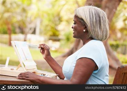 Senior Woman Sitting At Outdoor Table Painting Landscape